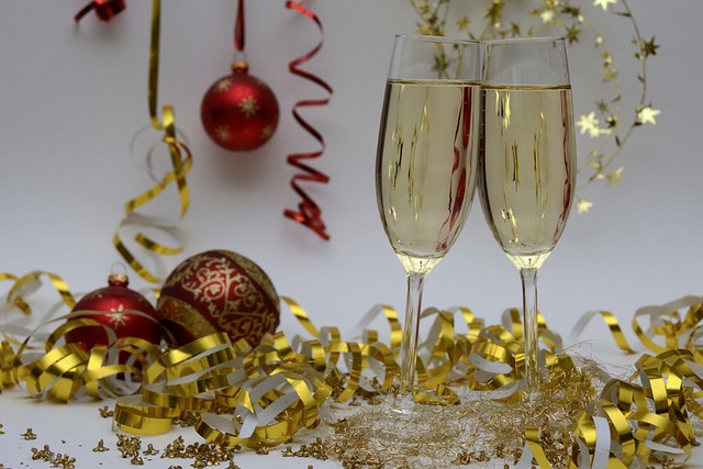 Two glasses of sparkling wine are with red baubles with gold tinsel. The words happy New Year is across the image.